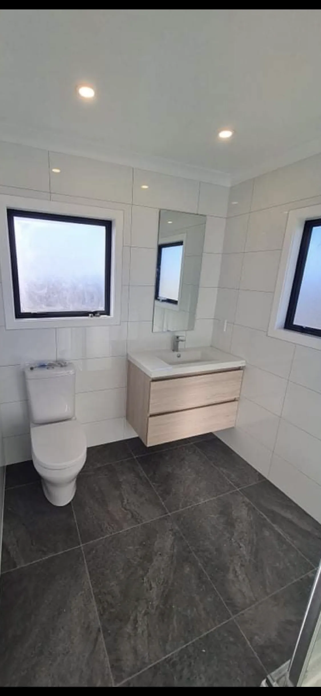 Modern bathroom renovation with wooden vanity, white tile, black framed windows and frameless shower